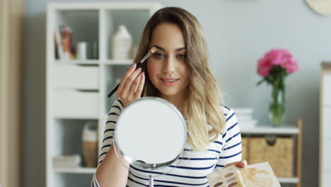 hermosa mujer maquillando los ojos mientras mira en un espejo de mesa