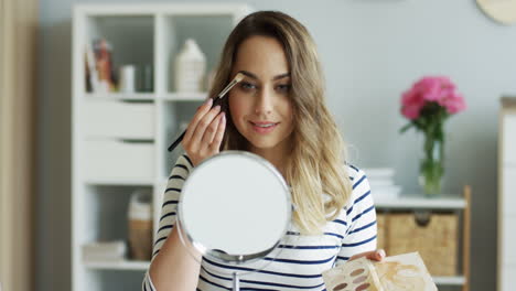 beautiful woman applying eye makeup while looking in a table mirror