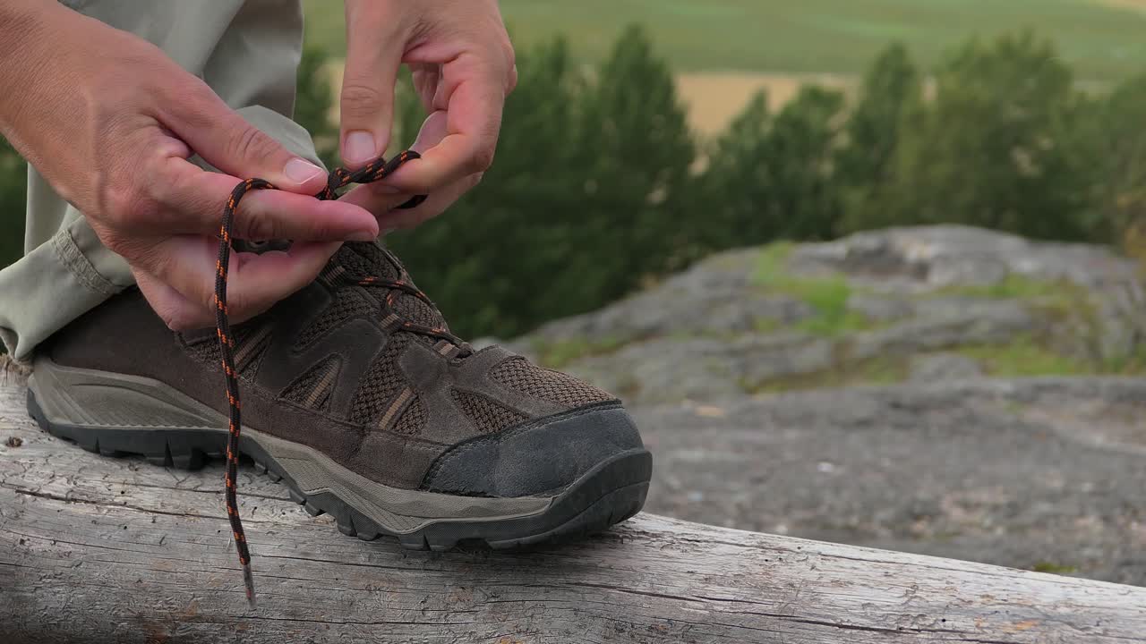 Un escursionista che allaccia i lacci delle scarpe da trekking in cima a una collina boscosa all'aperto.