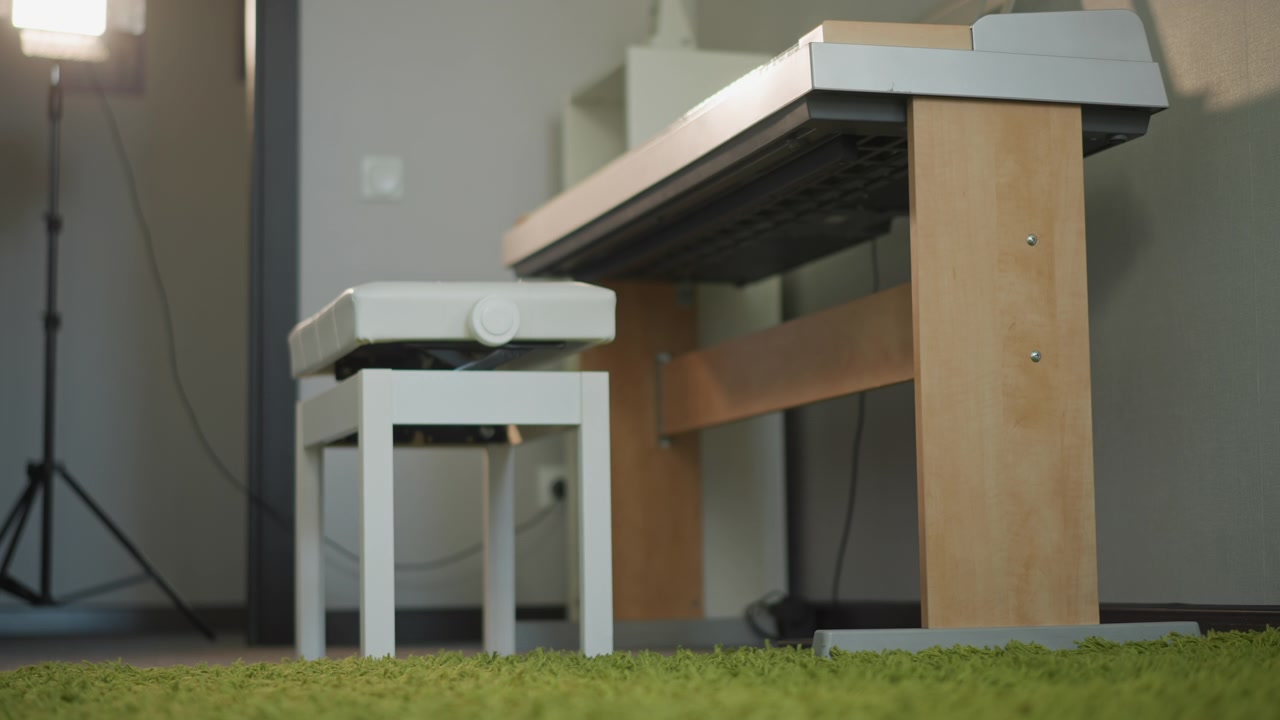 Panca bianca per tastiera su tappeto verde, accogliente allestimento per lezione di pianoforte per principianti in soggiorno illuminato dal sole, supporto in legno per tastiera e tappeto morbido, luce da studio e treppiede sullo sfondo, panca vuota che invita lo studente