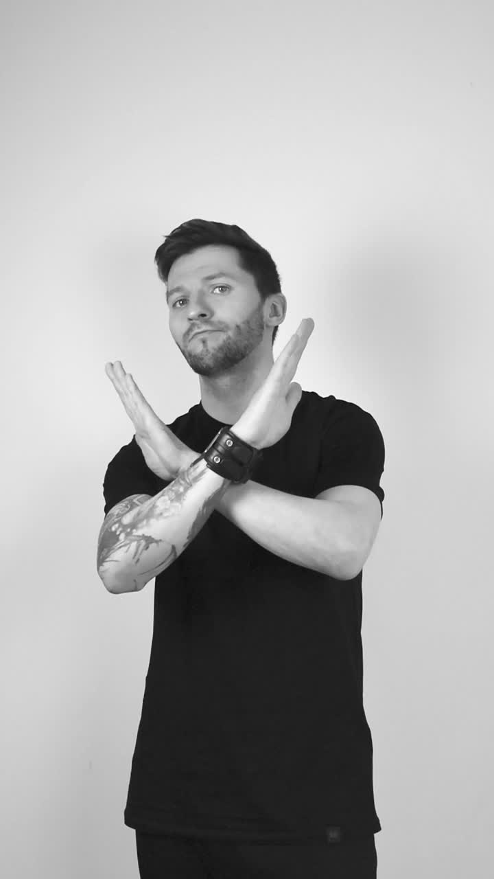 Grayscale footage of a man rotating and wavering his head back and fourth indicating he is not happy and crossing his arms showing you to stop whatever you are doing and he does not like it. Tattoos