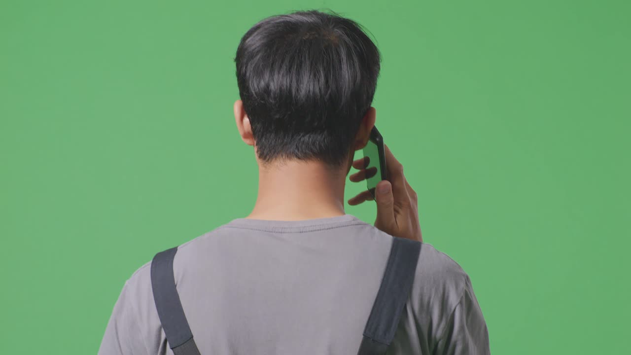 녹색 화면 배경 스튜디오에서 는 동안 스마트폰으로 이야기하는 아시아 남성 노동자