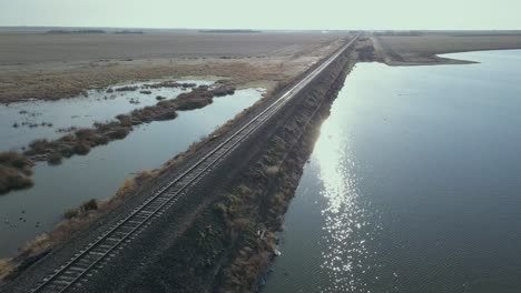 empty train tracks on the flat prairie with sun on a pond