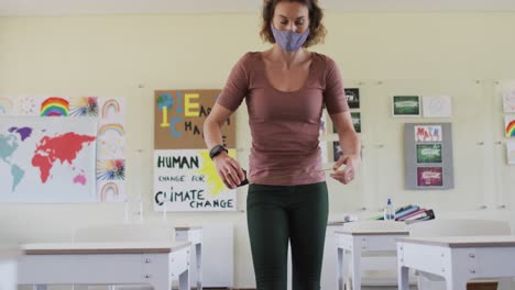 maestra con máscara de cara midiendo la distancia entre los escritorios en la clase en la escuela