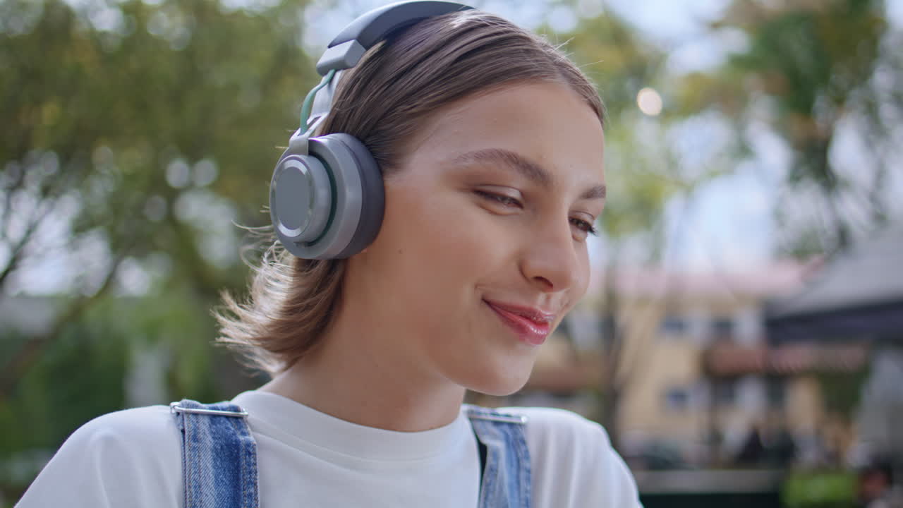 Lady talking video meeting wearing wireless headphones in sunny park closeup
