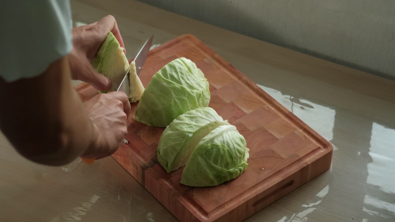 Hands and knife cutting the core off cabbage quarters on wooden chopping board. Static shot