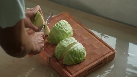 hands and knife cutting the core off cabbage quarters on wooden chopping board. static shot