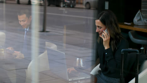 vista lateral de una hermosa mujer de negocios caucásica hablando por teléfono móvil y trabajando usando una computadora portátil