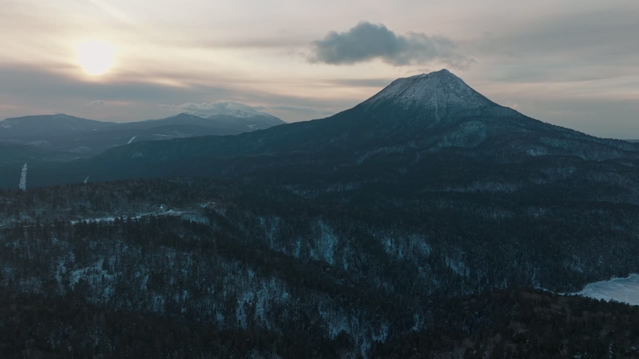 Mount Oakan Volcano At Sunrise Surrounded By Snowy Forest In Winter. - aerial pullback shot