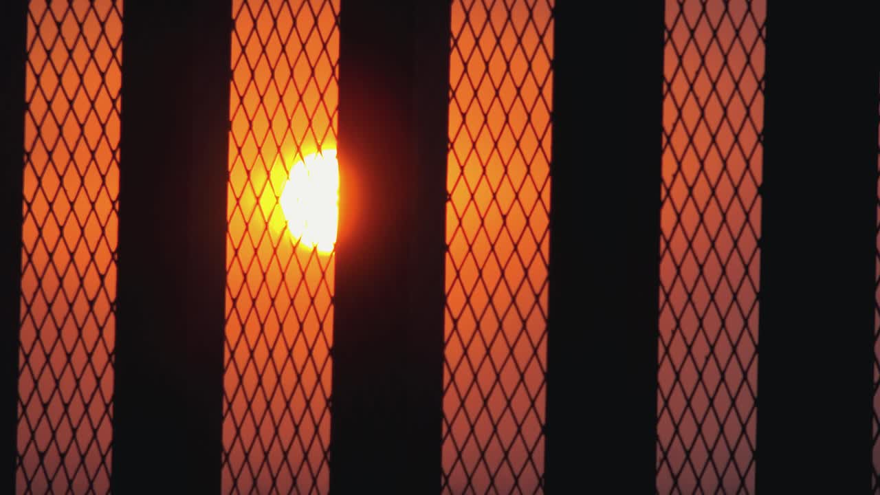 매우 가까운 울타리를 통해 해가 지는 것과 오렌지색 하늘의 넓은 저속 촬영