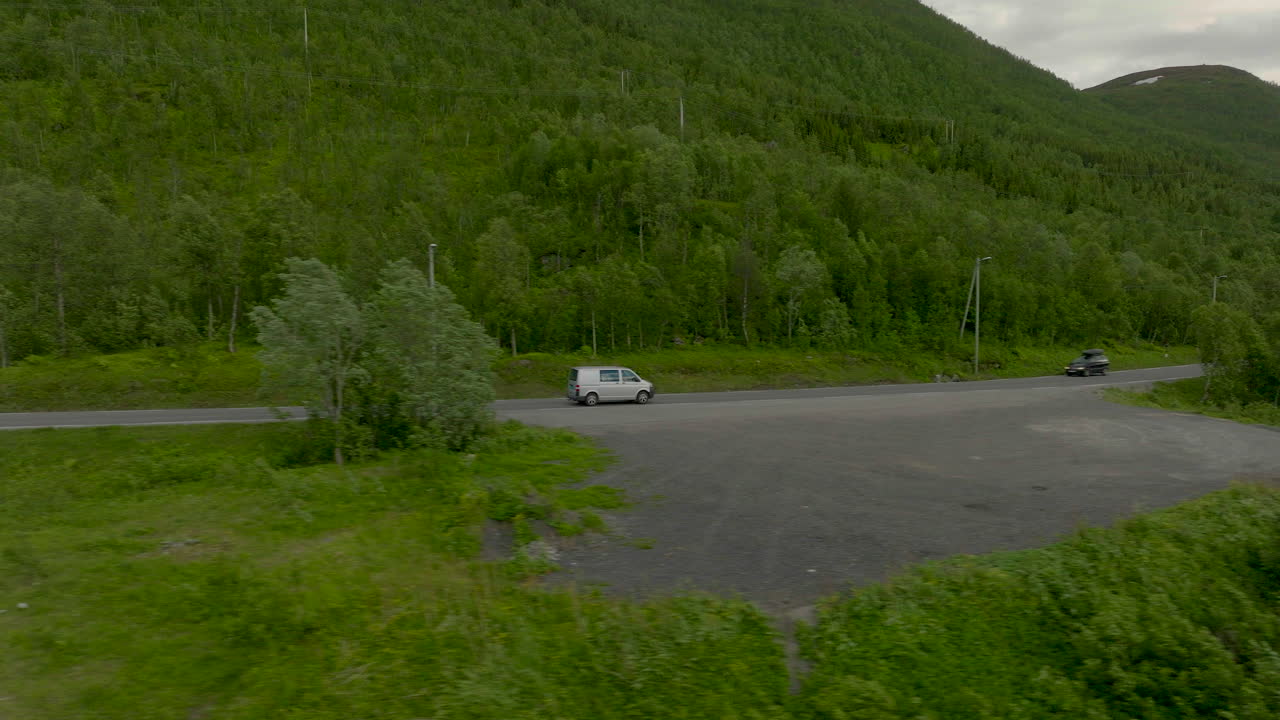 강을 지나는 숲이 우거진 산맥 기슭 도로를 여행하는 은색 밴