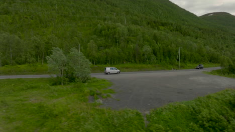 silver van travelling on road at base of forested mountain range passing a river