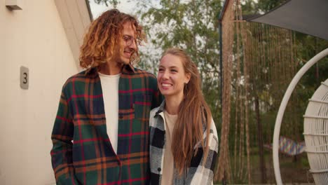 A-curly-haired-guy-in-a-checkered-shirt-is-chatting-and-walking-with-his-girlfriend-outside.-Rest-in-the-country-house