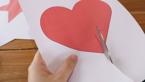 primer plano de manos cortando la forma de un corazón en papel con tijeras