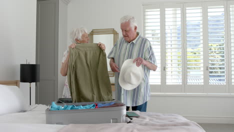 senior caucasian couple packing suitcase in bedroom at home, slow motion