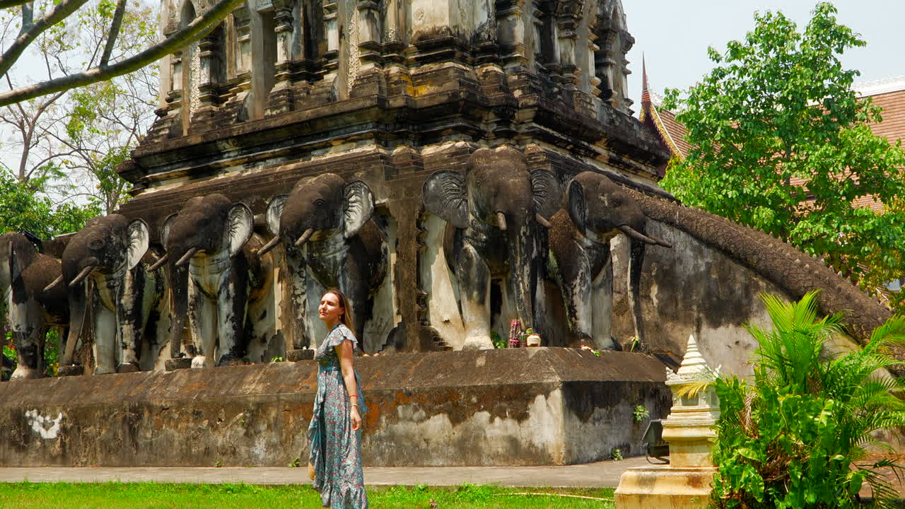 una chica rubia bonita con un vestido azul visitando un templo de piedra exótico en tailandia