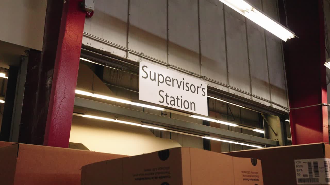 Camera pushes in on sign marking supervisor hub within busy industrial space