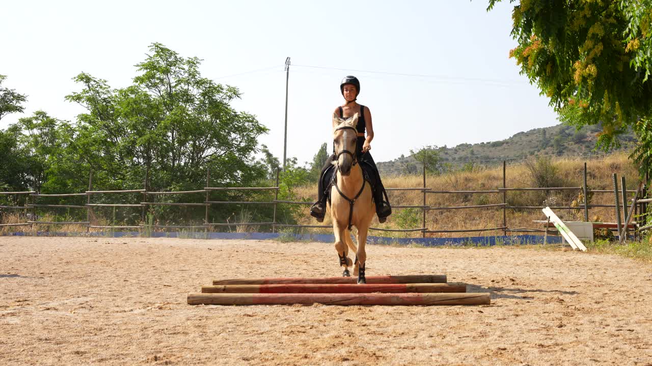 Frontal view of a white horse and female rider threading between three ground bars with control
