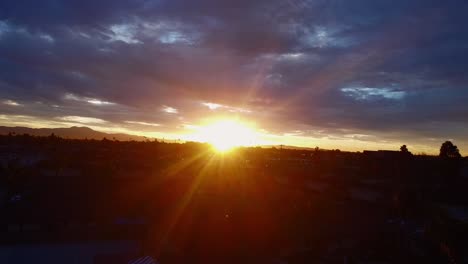 Sun-rays-shine-through-clouds-over-cityscape,-drone-shot