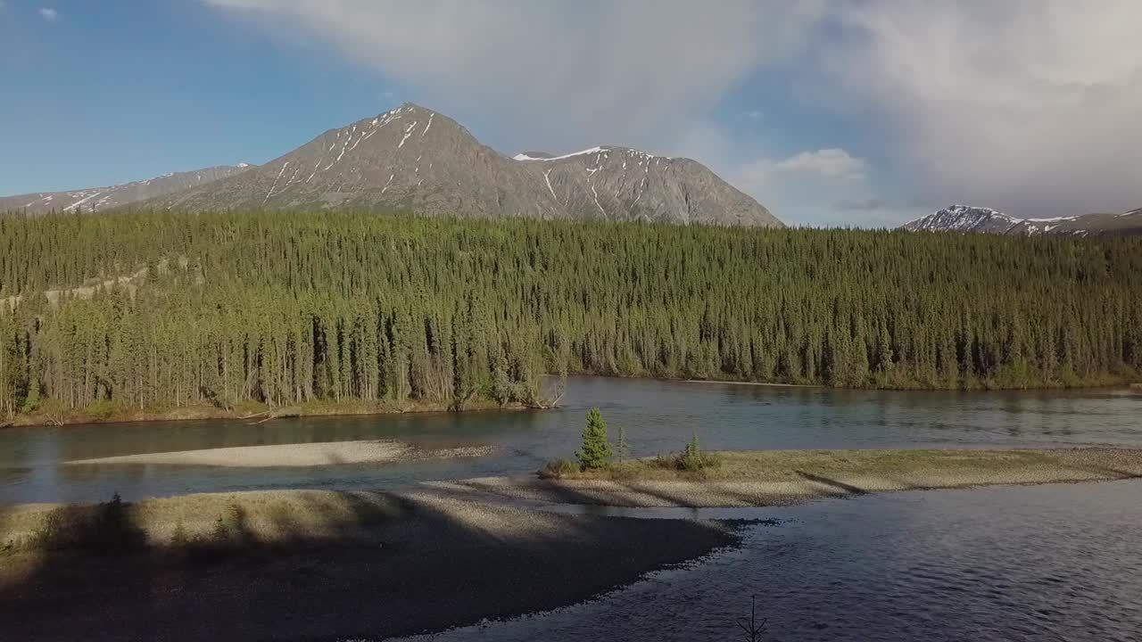hermoso vuelo hacia atrás en verano sobre el río yukon takhini con vista al bosque verde y la cordillera en el fondo al atardecer, canadá, drone aéreo retrocede