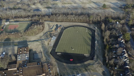 aerial view orbiting high school lacrosse field with track circling, 4k