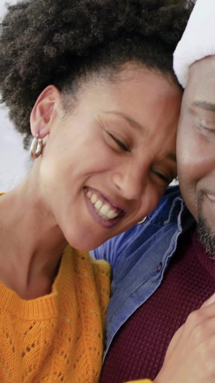 Video verticale: Donna in giallo che si appoggia al partner sul divano sorridendo, con una mano che accarezza la pancia, innamorata.