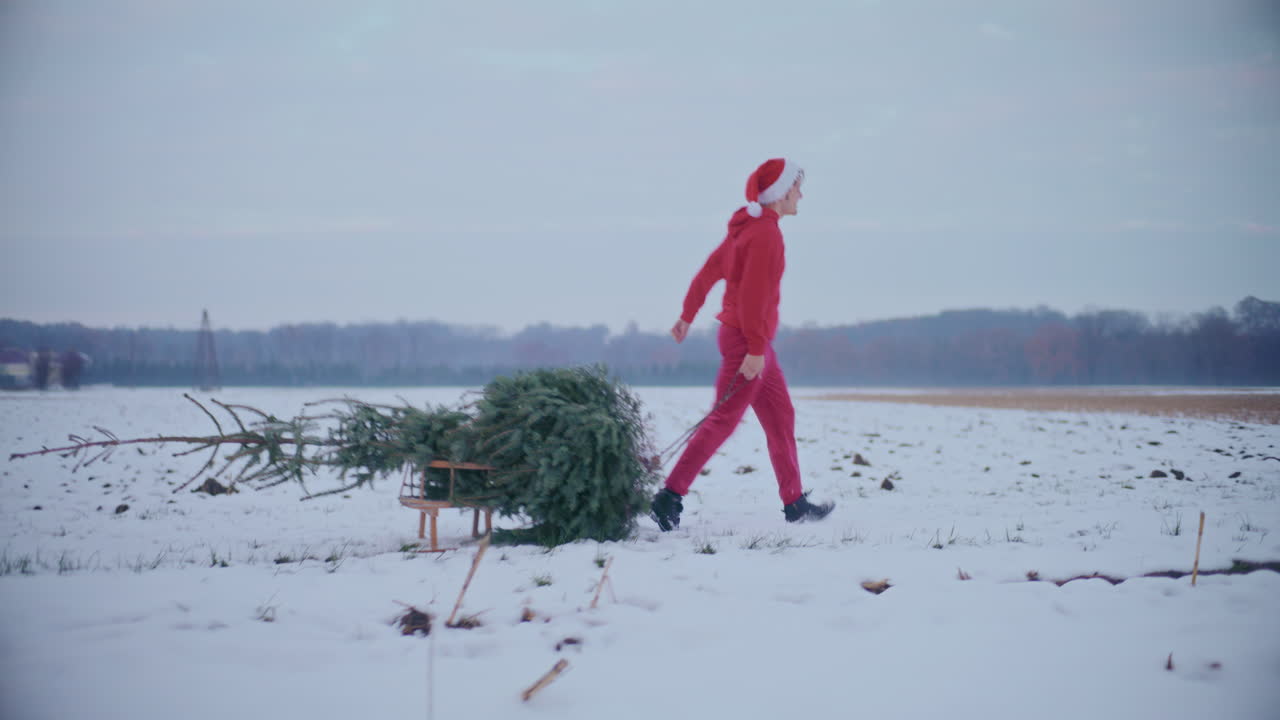 hombre alegre tirando del árbol de navidad en el paisaje cubierto de nieve