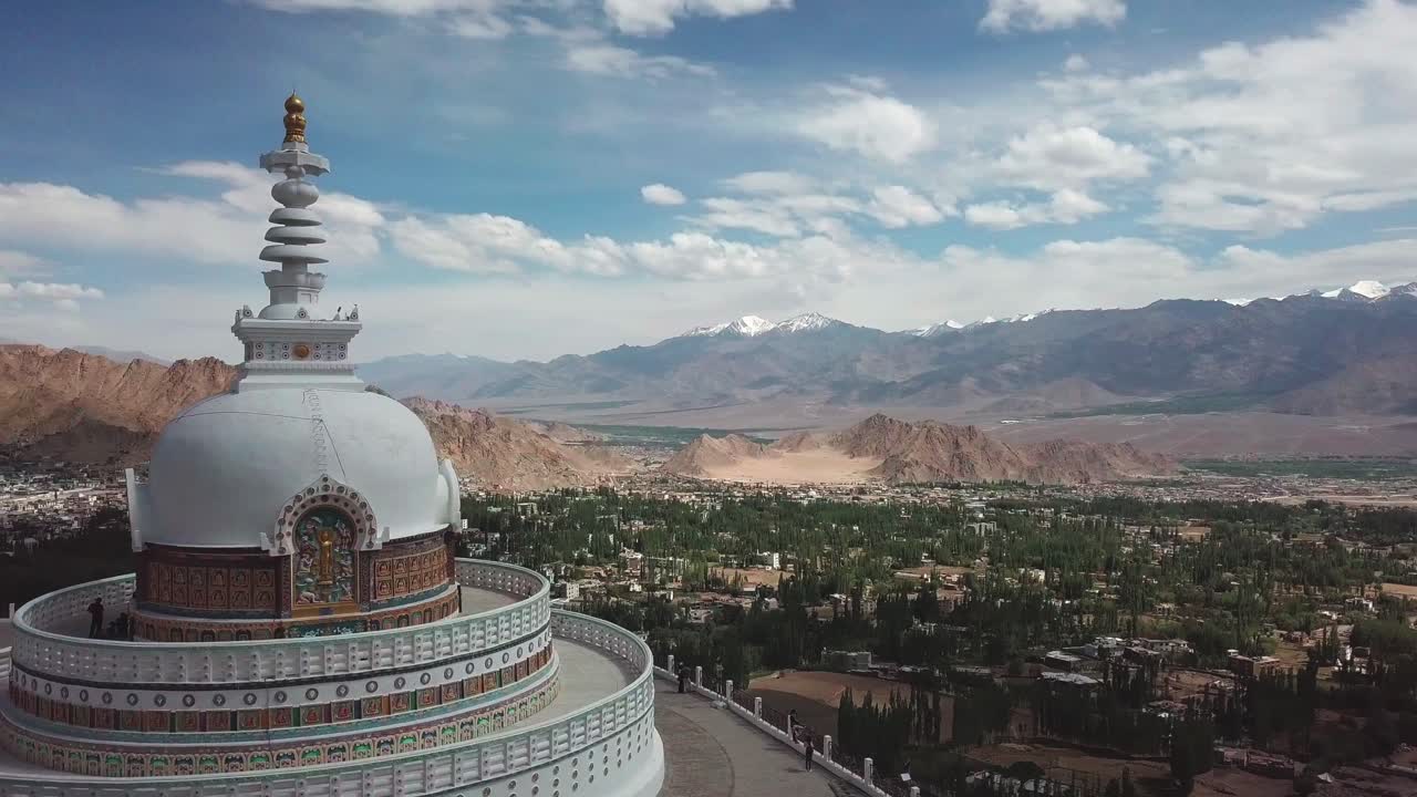 View of a Himalayan town and a buddhist temple with blue skies and white clouds and dry arid mountain scenery.