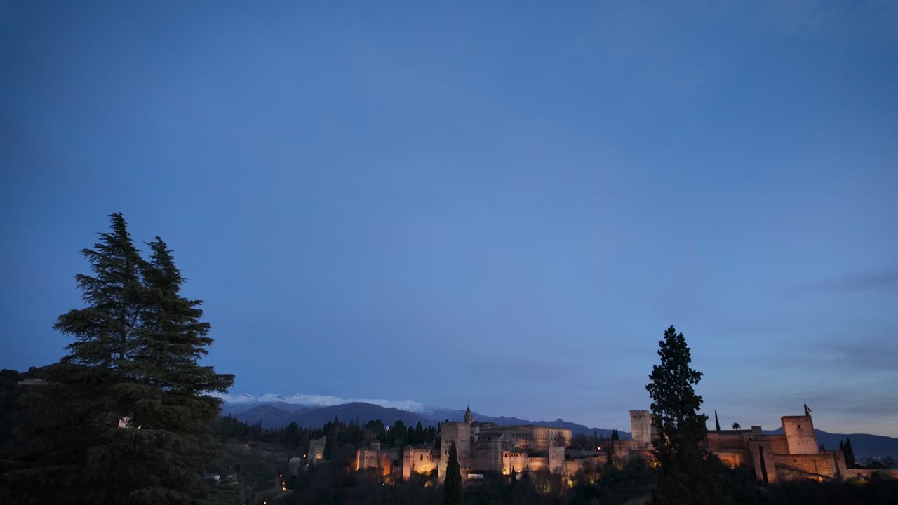 Panoramic hyperlapse of the Alhambra, Sierra Nevada and the city of Granada during sunset, capturing the smooth transition from daylight to night over this iconic Andalusian landscape