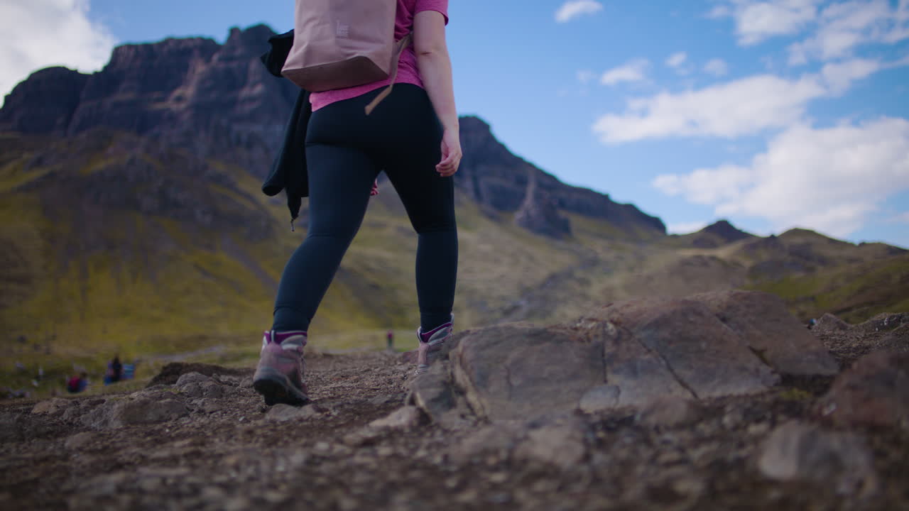 mujer mochilera caminando por el campo escocés, el storr en el fondo