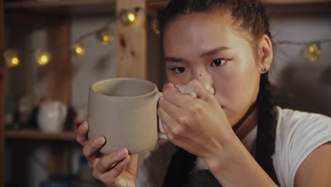 young woman potter smoothing the border of the cup handle using a tool