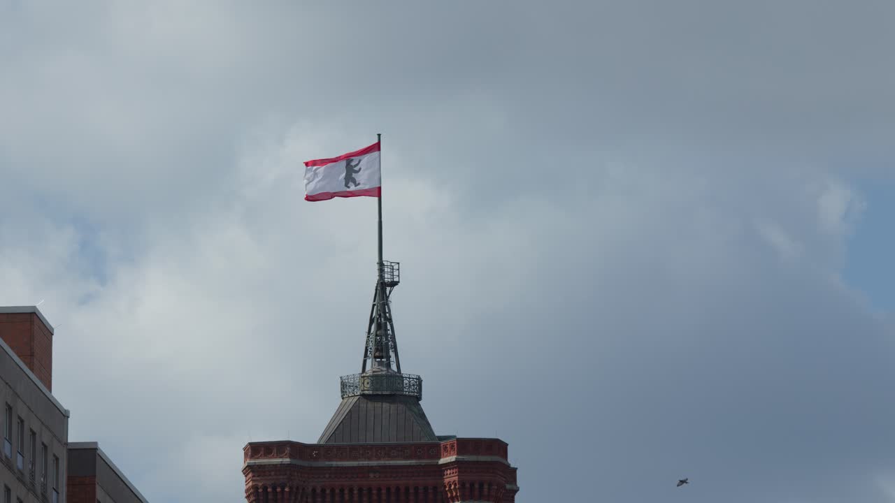 Berlin city flag waves atop historic Rotes Rathaus under cloudy sky, static camera, natural light