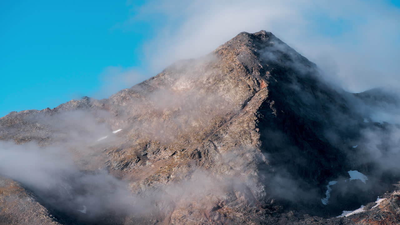 Mountain peak shrouded in moving clouds during clear sky timelapse