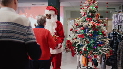 employee wearing santa claus suit holding raffle contest in christmas decorated shopping mall clothing shop during winter holiday season, inviting elderly couple to participate