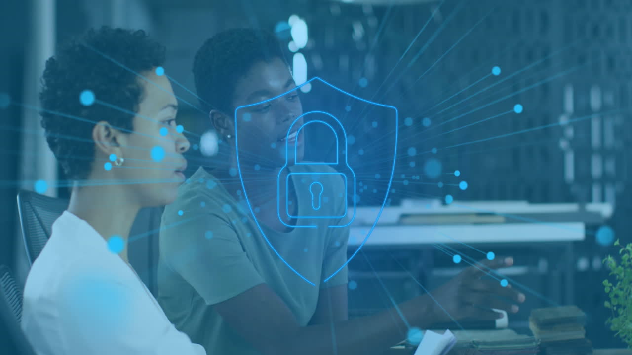 Animation of padlock in shield over diverse female coworkers discussing reports on laptop in office