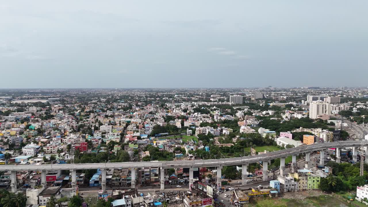 Vista aerea di un denso agglomerato urbano attraversato da un enorme cavalcavia sopraelevato. Sullo sfondo, moderni grattacieli contrastano con le case basse sotto un cielo nuvoloso.
