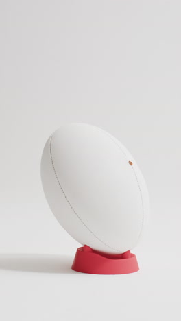 Vertical video of white rugby ball on kicking tee on white background with copy space, slow motion