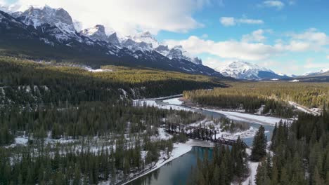 aerial pan of alpine railroad bridge with river, mountains and forest