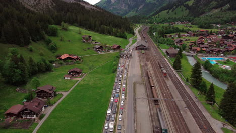 Luftaufnahme-Von-Autos-Und-Zügen,-Die-An-Der-Einfahrt-Zum-Bergtunnel-Lötschbergtunnel-In-Der-Schweiz-Anstehen