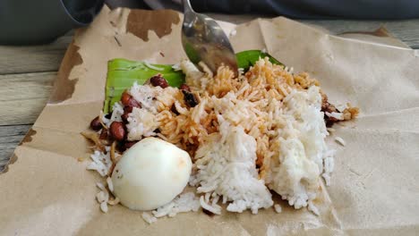 a woman enjoys nasi lemak bungkus, malaysia's popular, quick breakfast. this simple meal, with egg and sambal, comes conveniently wrapped in paper for easy portability