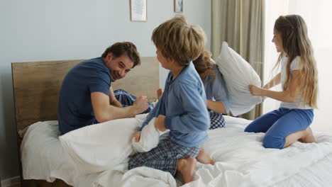 cute little children having fun and fighting with pillows with their parents in bed with pillows in the morning