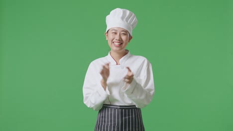 la mujer chef asiática sonriendo y aplaudiendo sus manos mientras está de pie en el estudio de fondo de la pantalla verde