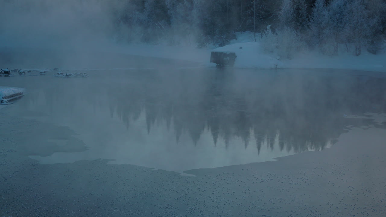 Frosty morning mist rising from cold alpine woodland frozen lake, Norbotten