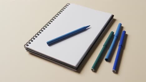 Close-up-of-notebook-with-blue-markers-on-beige-background,-in-slow-motion