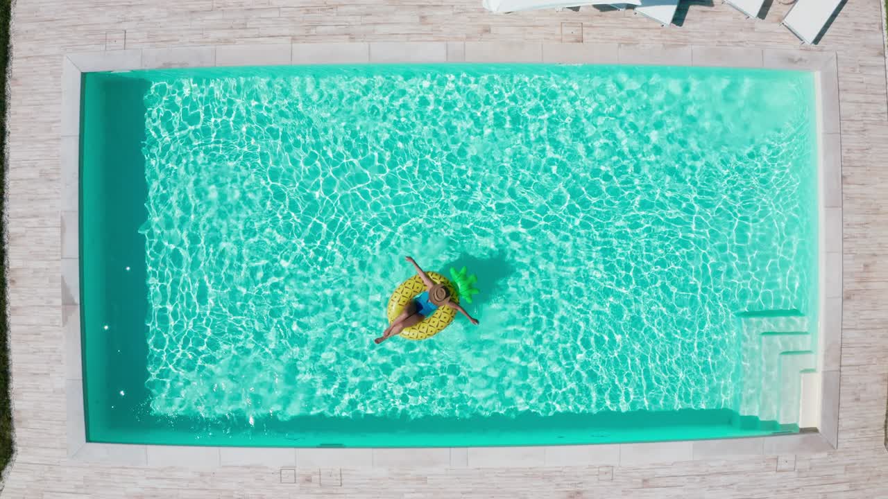 Rekaman drone 4K seorang wanita mengambang di pelampung tiup kuning di kolam renang.