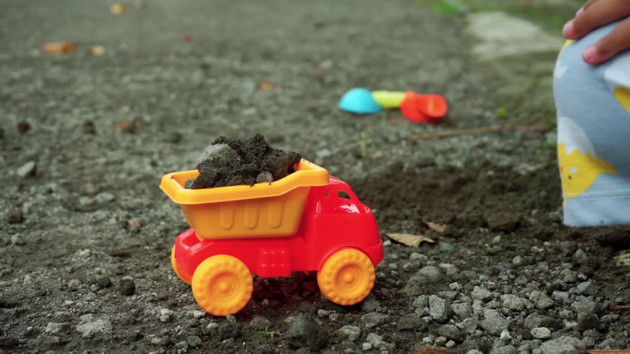 mano de niños juegan con piedra, camión de juguete y arena