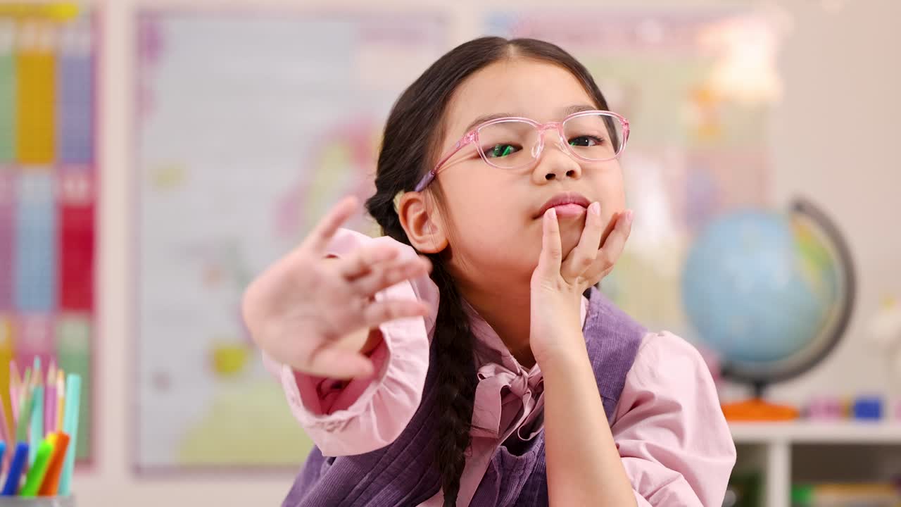 Confident schoolgirl in classroom extends hand in stop gesture, colorful supplies, soft even lighting