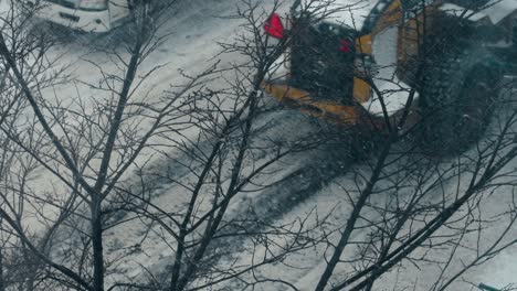 Yellow-Snowplow-Truck-Cleans-Road-in-front-of-Leafless-Branches-4K