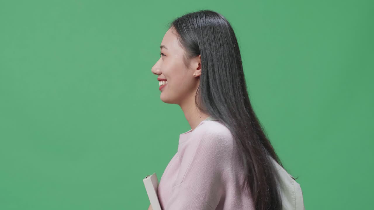 책 을 들고 녹색 스크린 스튜디오 에서 고 있는 아시아 여성 학생 의 측면 시각