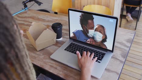 Mixed-race-man-sitting-in-cafe-using-laptop-making-video-call-with-friends